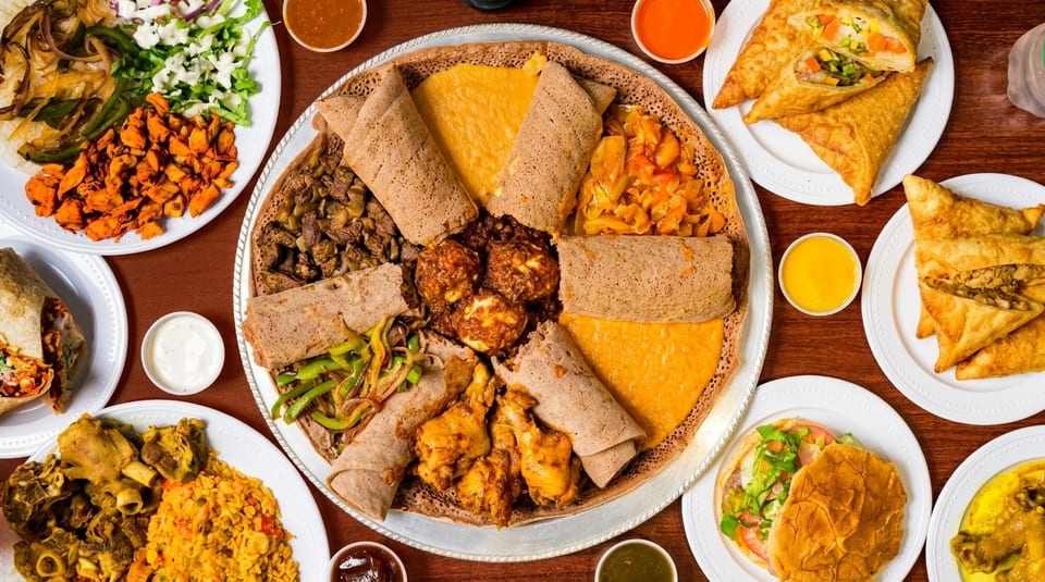 Overhead view of a large platter of Ethiopian injera with various stews, surrounded by other dishes.